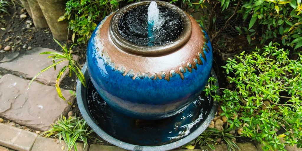 A DIY water fountain outdoors with a plant inside it. 