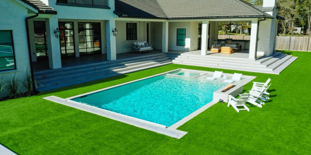 A swimming pool located in a backyard, surrounded by green grass and some plants. 