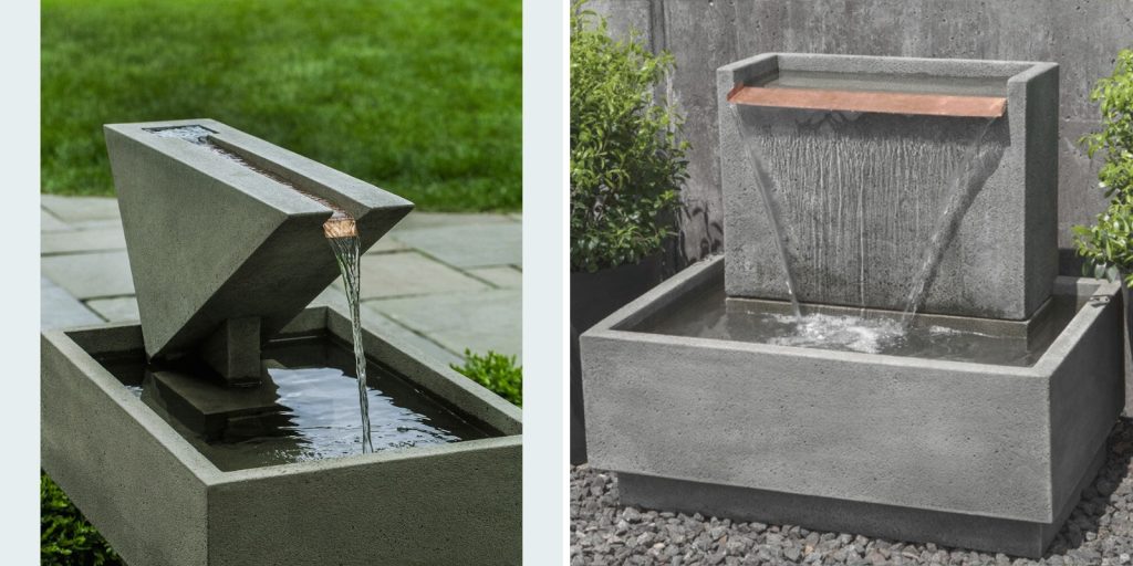 A couple of water fountains in a garden with plants and grass surrounding it.