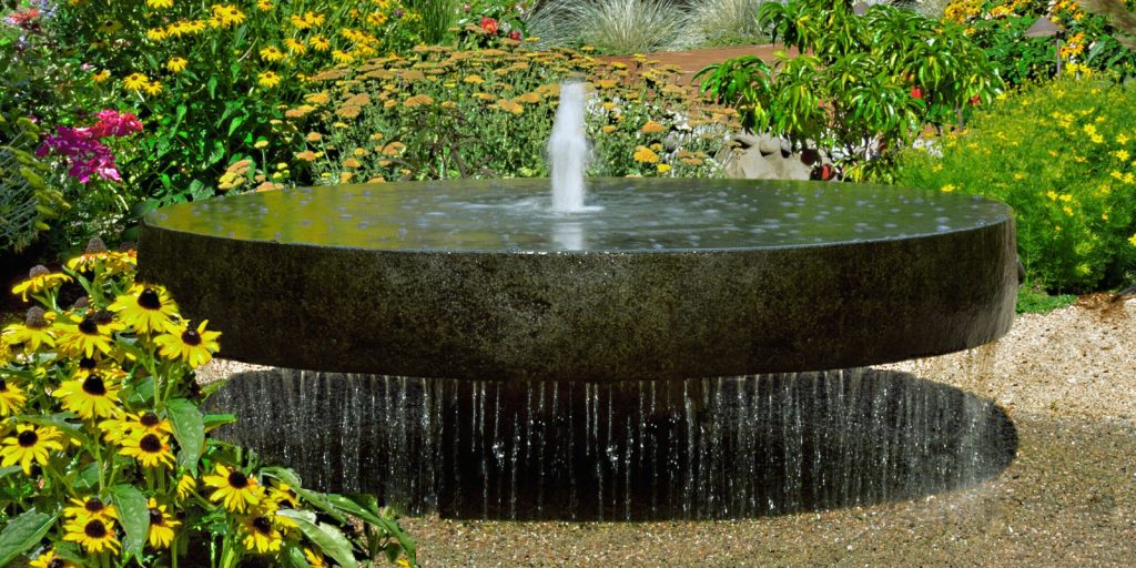 A water fountain in a garden surrounded by flowers and plants.