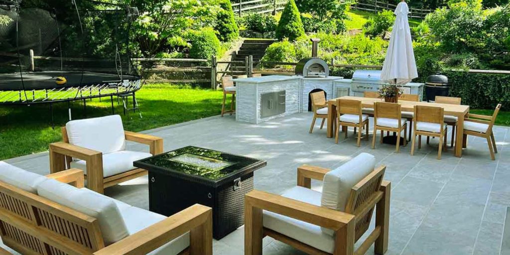 Patio with chairs and a grill, surrounded by plants and trees. 