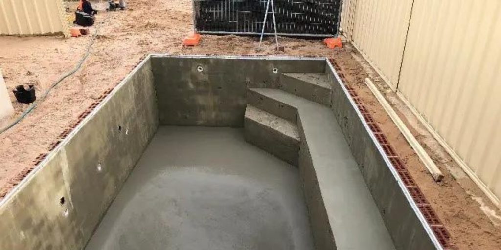 An indoor swimming pool concrete foundation with a fence around it