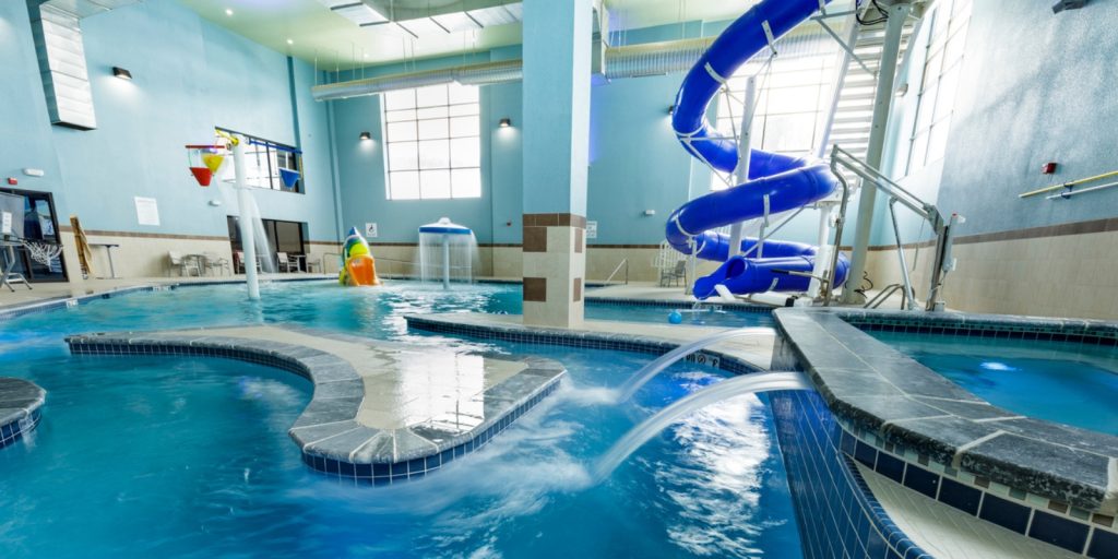  An indoor swimming pool with a slide. It features clear blue water.