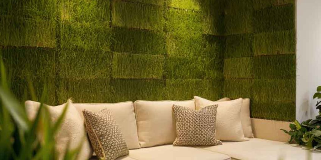 A couch with pillows in an indoor setting and behind accent grass wall