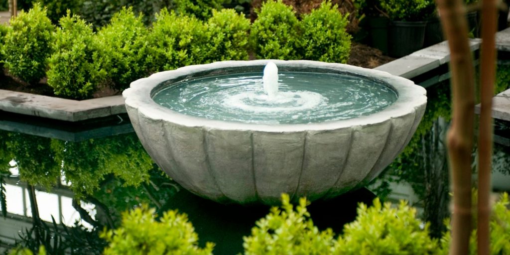 A round water fountain located outdoors in a garden. 