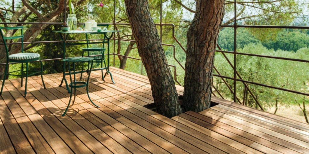 A deck area furnished with a table and chairs, surrounded by a tree.